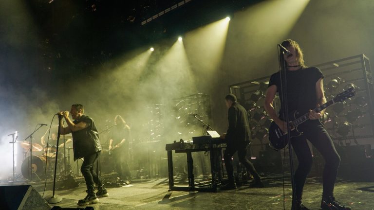Trent Reznor performing onstage at Nine Inch Nails announcement; dramatic lighting with crowd visible in foreground