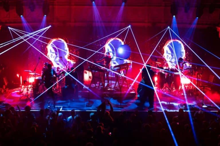 Faithless performing live on stage with immersive lighting at a large outdoor venue.