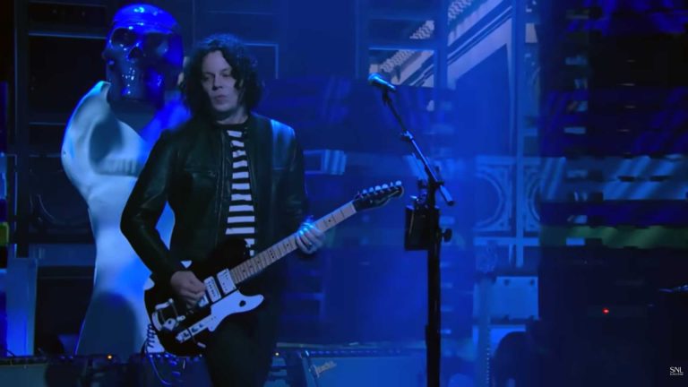 Jack White performing live with a blue guitar, highlighting his upcoming SNL musical guest appearance.